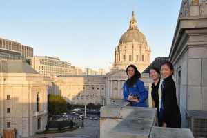 Fr&aring;n v&auml;nster till h&ouml;ger: Erin Battrick, Emily Pan och Michelle Wu med San Franciscos City Hall i bakgrunden p&aring; balkongen av War Memorial Opera House.