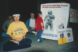 De eerste dag van een hongerstaking tegenover de ambassade van de volksrepubliek China in Londen, 2001. Ben Chen's moeder (links voor) doet mee aan de hongerstaking. Een dreumes kijkt naar een foto van een baby die vermoord werd vanwege de vervolging van Falun Gong in China.
