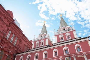 Красные стены и шпили с позолоченными эмблемами на Кремле на фоне голубого неба.