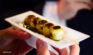 Auf der anderen Seite der Welt beißen unsere Tänzer in japanische <i>aburi-mochi</i>, gegrillte Reiskügelchen auf Bambusspießen - eine tausend Jahre alte Süßigkeit aus Kyoto.
