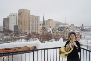 與此同時，一場強降雪給底特律披上了一層銀妝素裹。神韻藝術團法國號演奏員Chi-Chien Weng 在戶外熱身。（攝影：Grace Mo）