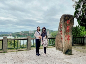 La presentatrice Nancy Zhang (a sinistra) e il soprano Rachael Bastick in posa vicino a una roccia imponente. Riesci a leggere o indovinare i tre caratteri scritti? (suggerimento: il nome del lago, ma in cinese).
