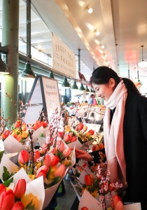 Te midden van de drukte van de beroemde Pike Place Market in Seattle, neemt danseres YuHui een moment om de schoonheid van de levendige bloemen te bewonderen. Heeft u nog nooit van de Pike Place markt gehoord? Denk maar eens aan Starbucks.