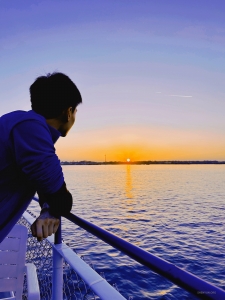 Mit der sanften Brise in den Haaren und der Wärme der Sonne auf der Haut genießt der Künstler den Glanz eines atemberaubenden Sonnenuntergangs auf dem Meer.