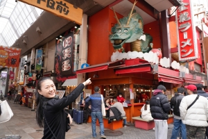 大阪の食で知られる道頓堀で、奇抜な龍の看板にみとれるカリーナ・フ。味覚だけでなく視覚にも訴えるレストラン街。巨大なカニや眩いネオンサインが店舗の上に掲げられている。
