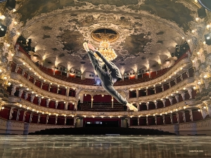 Against the opulent Neo-Rococo backdrop of the Prague State Opera, a dancer performs a flawless zi jin guan—a 'purple-gold crown' jump—an essential technique for female classical Chinese dancers.